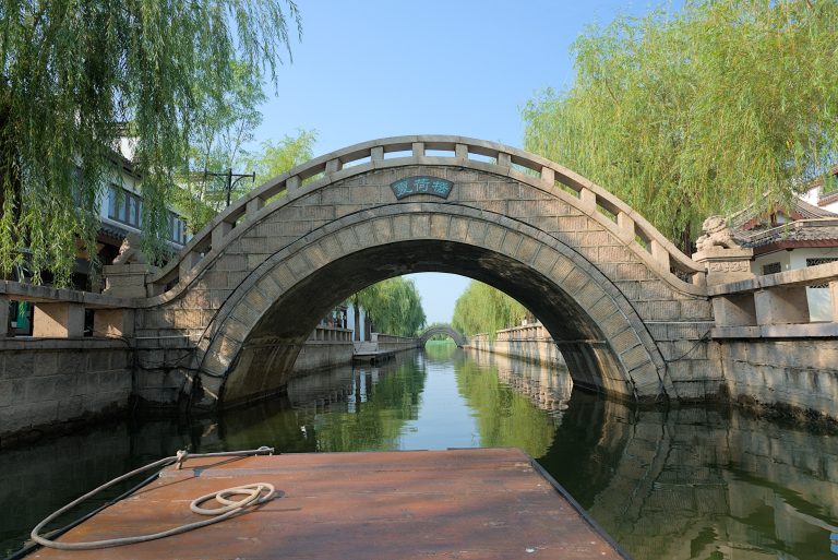 A serene scene of an ancient bridge over a calm river, with reflections of the bridge in the water.