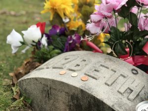 View larger photo: The gravestone of Lizzy Borden in Fall River, Massachusetts: a simple arched stone with Elizabeth carved onto the top. 3 coins are placed on top and colorful flowers are planted around. 