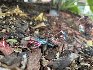 Red, white, and blue garland in the shape of stars, strewn across mulch on the ground.