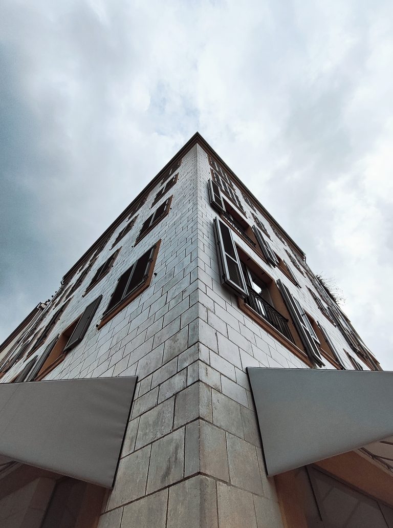 Symmetrical picture of the corner of a building, taken from low angle. A cloudy sky is visible above the building.