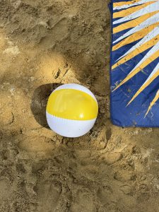 View larger photo: A beach ball and a dark blue blanket on a beach, seen from above.