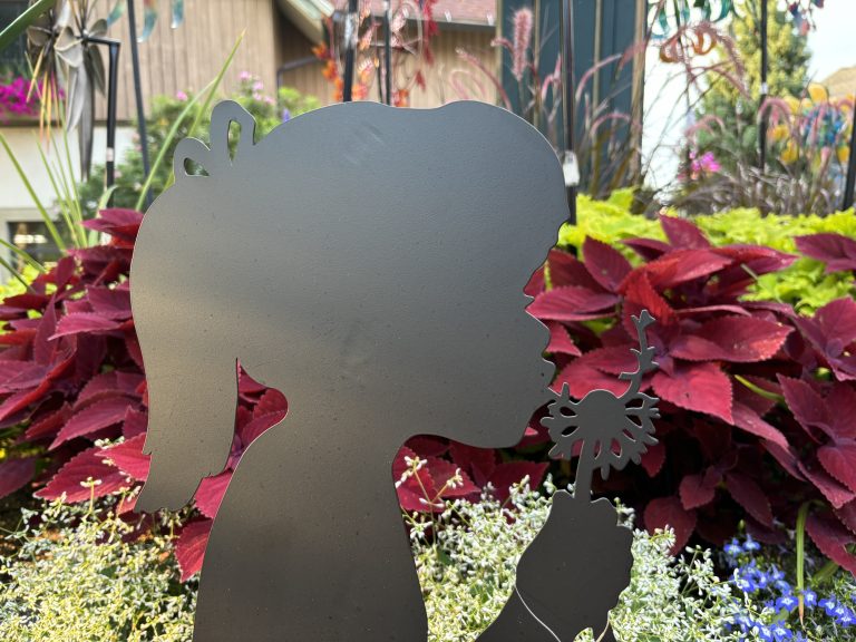 Steel silhouette of a child blowing on a dandelion.