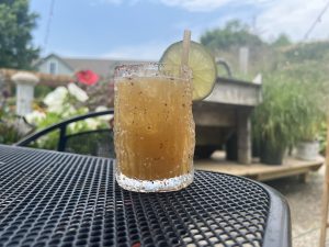  Hot Honey Peach Margarita sitting on a mesh metal patio table with a garden in the background (The Station on Kings, Lewes, Delaware)
