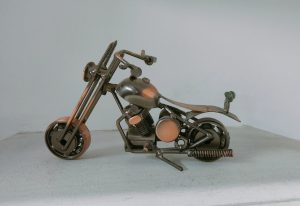 A miniature, handmade motorcycle sculpture made from various metal components, including screws, bolts, and nuts, displayed on a white surface against a plain background.