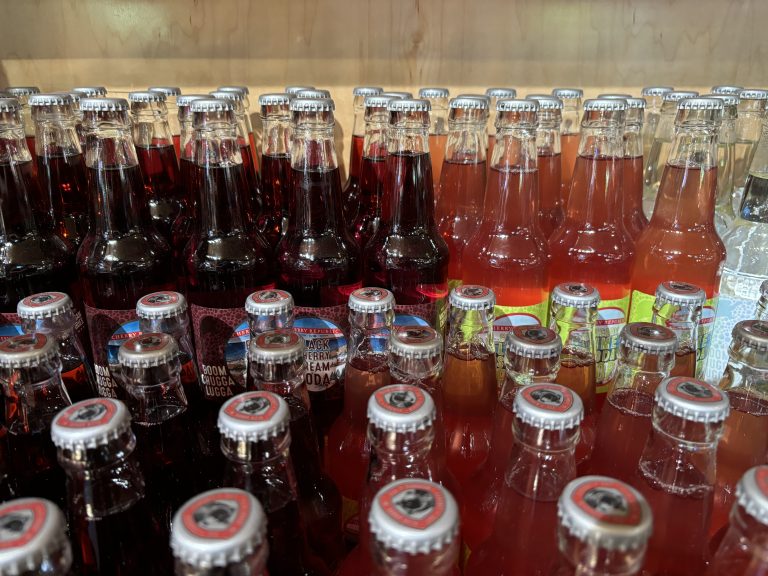 Rows of multicolored glass drink bottles with metal tops.