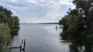 View of the Starnberger See, Bavaria, Germany. Green trees can be seen on both sides. Several small boats are visible on the water, as well as a single water bird.