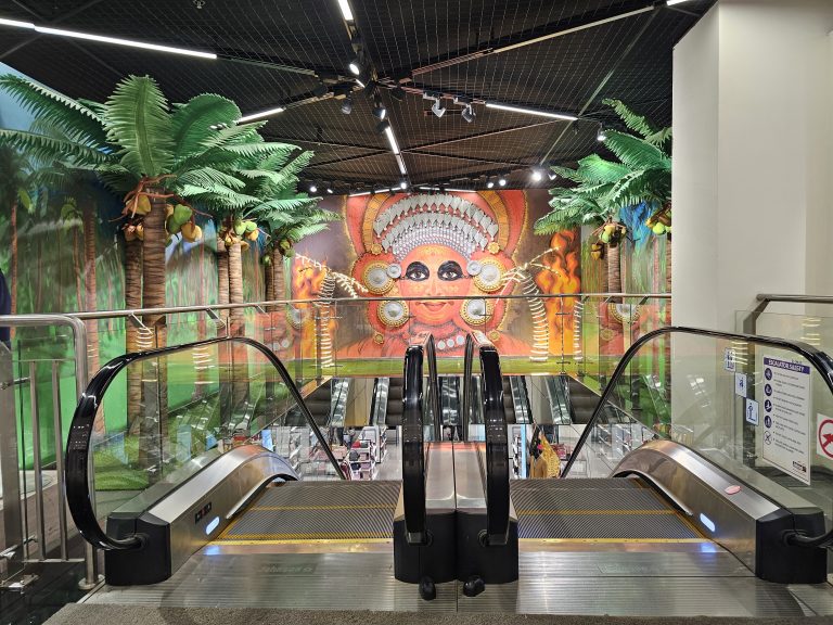 An escalator in a shopping mall leads up to a colorful mural of Theyyam, a popular ritual form of worship of North Malabar in Kozhikode Kerala, India.