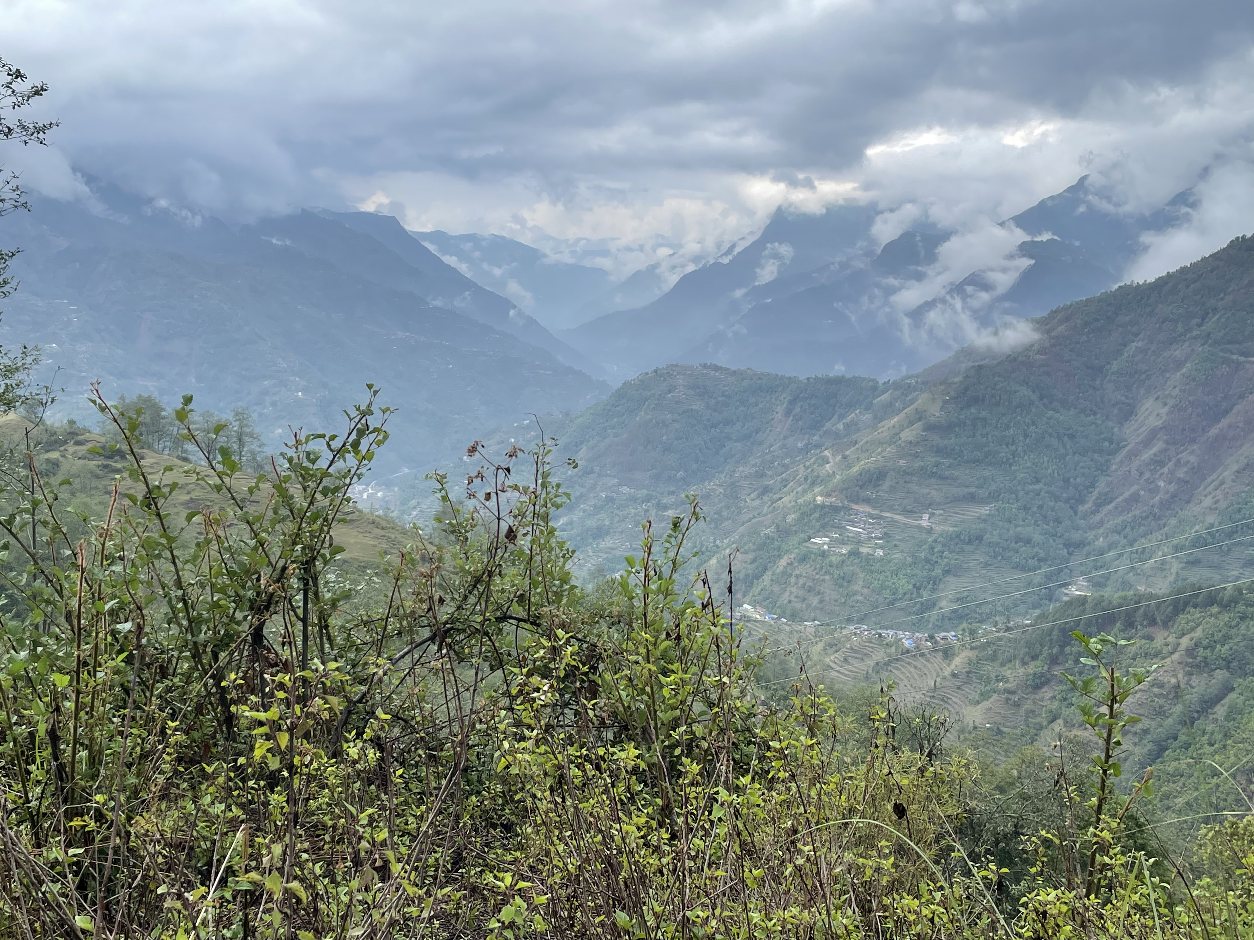 Monsoon season clouds covering mountains in the distance. Some green bushes are visible in the foreground.