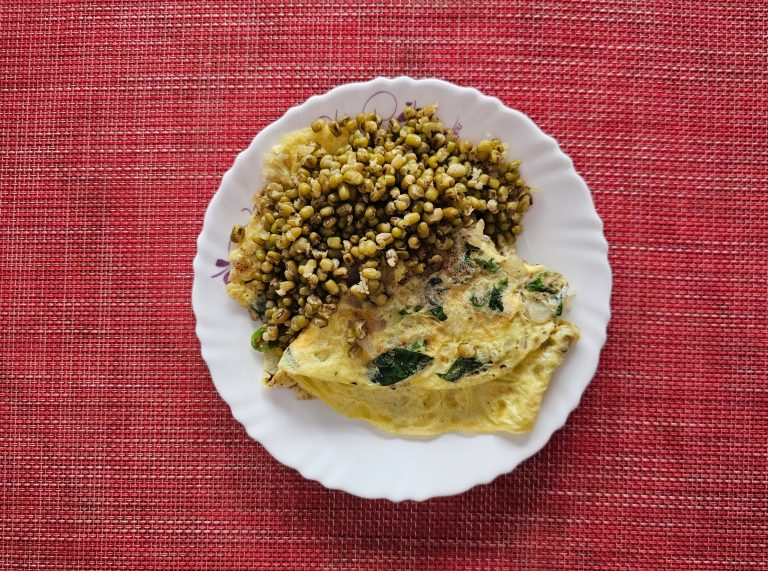 An omelet and a side of cooked mung beans on a white plate. The plate is on a red tablecloth.