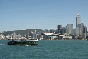 View larger photo: A ferry is crossing the harbour in Hong Kong. The ferry is green with a white band making it recognisable as the historic Star ferry. In the background the mountains meet a pale blue sky with the city buildings laid out in the mid-ground.