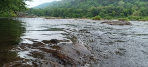 Landscape view of a water flow through river rocks and the background contains trees and sky