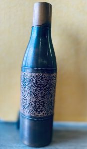 A blue copper bottle on a table. The bottle has ornate etchings.