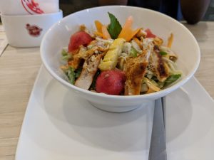 A white bowl full of fresh salad with chicken, watermelon and pineapple pieces on top.