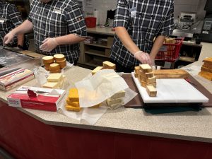 View larger photo: People cutting and packaging cheese in a cheese store.