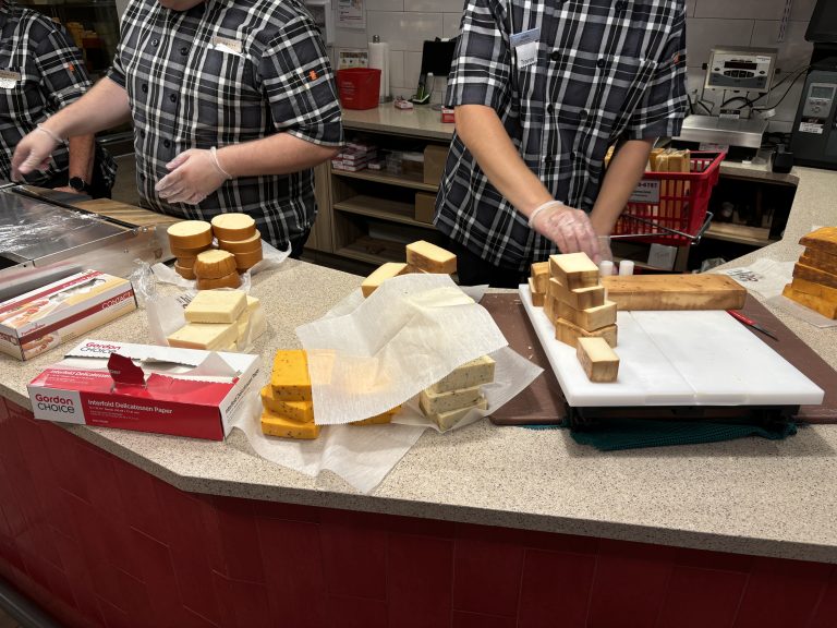 People cutting and packaging cheese in a cheese store.