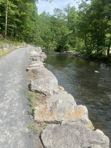 View larger photo: Trail walk way with a stone wall edge next to a stream of water. 