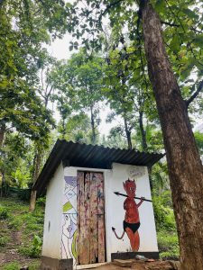 Luttappi, a child-like devil cartoon charater, is painted on the side of a small white building in a forest. The building has a corrugated metal roof.