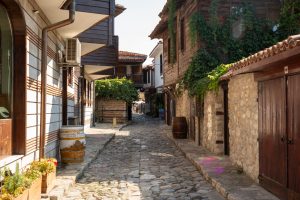 A narrow street in Old Nessebar, Bulgaria, with stone and wood buildings on either side.