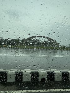 Rain droplets on a car window with a blurred background of an empty road and a structure in the distance.