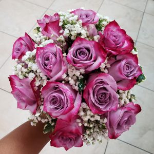 Close-up of the top of a hand-tied, circular-style bridal bouquet with purple roses and baby's breath.