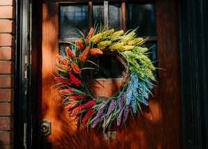Decorative wreath on a door, comprised of flowers in a rainbow pattern.