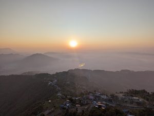 View larger photo: Sunrise above misty mountains in Pokhara Nepal, with residential buildings and a construction site in the foreground.