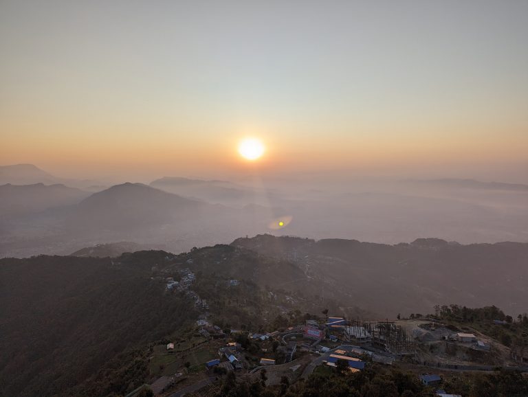 Sunrise above misty mountains in Pokhara Nepal, with residential buildings and a construction site in the foreground.