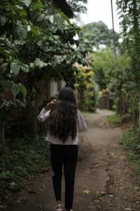 View larger photo: A girl walking through a path by speaking on the phone.The surrounding area is lush and green, suggesting a natural or garden setting.