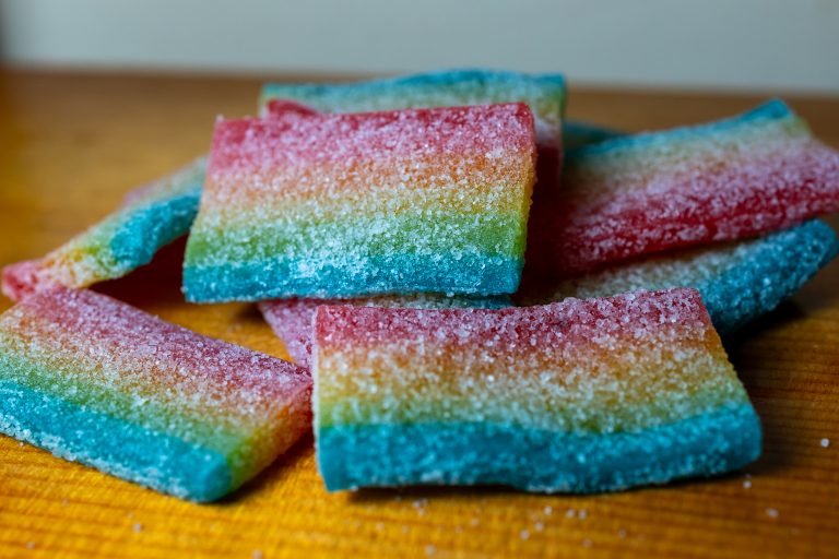 A pile of rainbow flag sugar coated candies on a piece of wood with a white background.