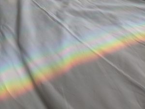 View larger photo: Rainbow reflected over a white bed blanket.