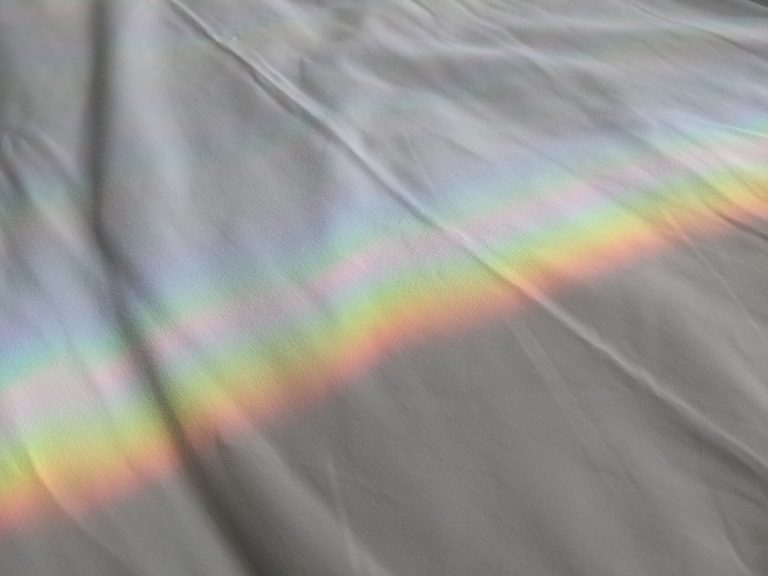 Rainbow reflected over a white bed blanket.