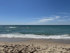 View larger photo: Waves on a sandy beach on the shore of Lake Michigan. People play in the surf in the distance.