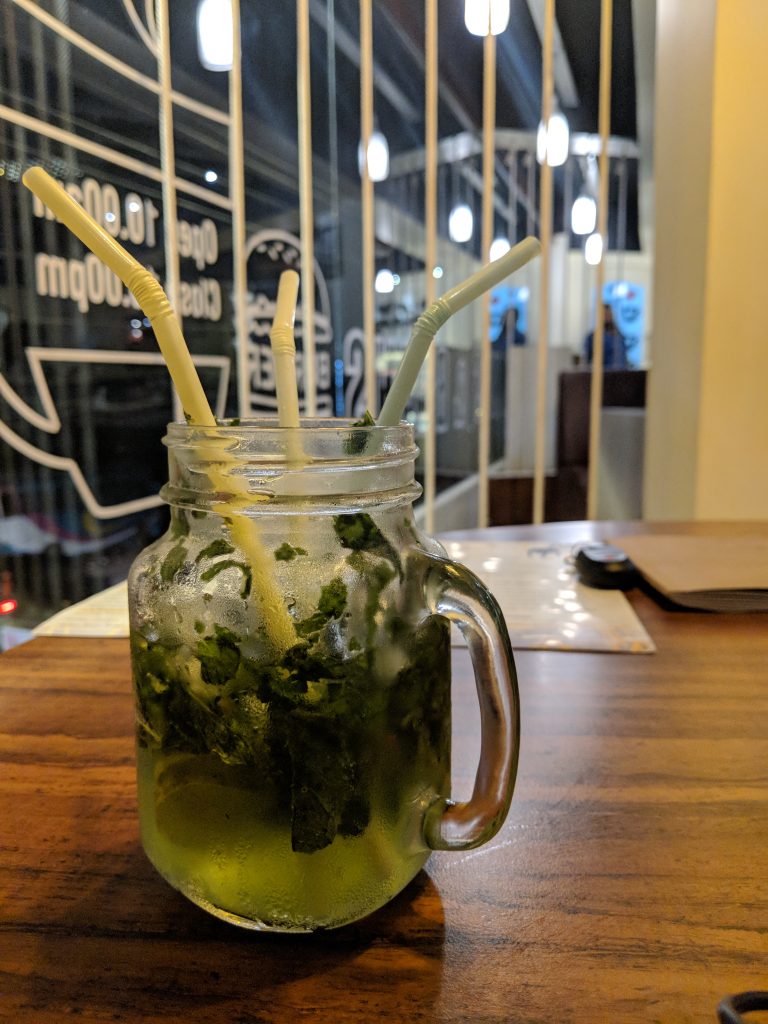 A mason jar glass filled with mojito and ice on a wooden table. There are three straws in the glass.