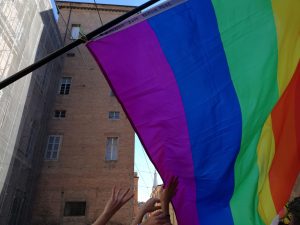 Hands raised up toward a rainbow flag with buildings in the background