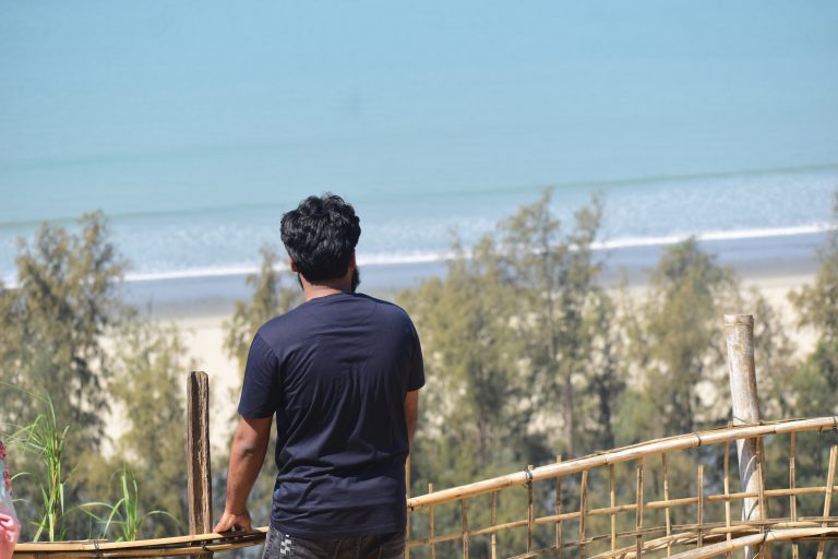 A man looks out over the ocean from behind a wooden fence.