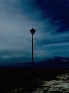 Public street lamp dark in the night, silhouetted against a lighter sky.