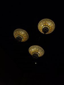 View larger photo: Three intricately patterned and illuminated dome-shaped lamps hang from a dark ceiling, casting a soft yellow glow.