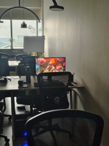 View larger photo: Bright computer screen on a table in a drab room full of other tables.