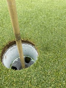 A close up of the cup and flagstick on a golf course green. There’s a ball mark dimple just outside the edge of the hole.
