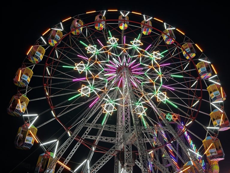 A brightly lit Ferris wheel at night with colorful neon lights in star shapes and multicolored passenger cabins.