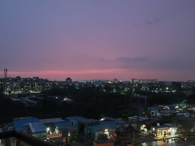 Sunset View of Pune from a balcony. Commercial buildings can be seen in the foreground, residential buildings in the distance. Soft shades of pink color the sky.