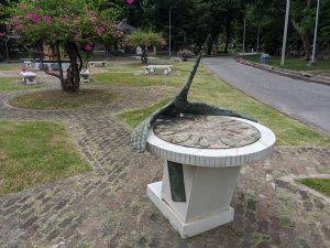 A sundial sculpture with a bird figure on a pedestal in Lumphini Park, Bangkok