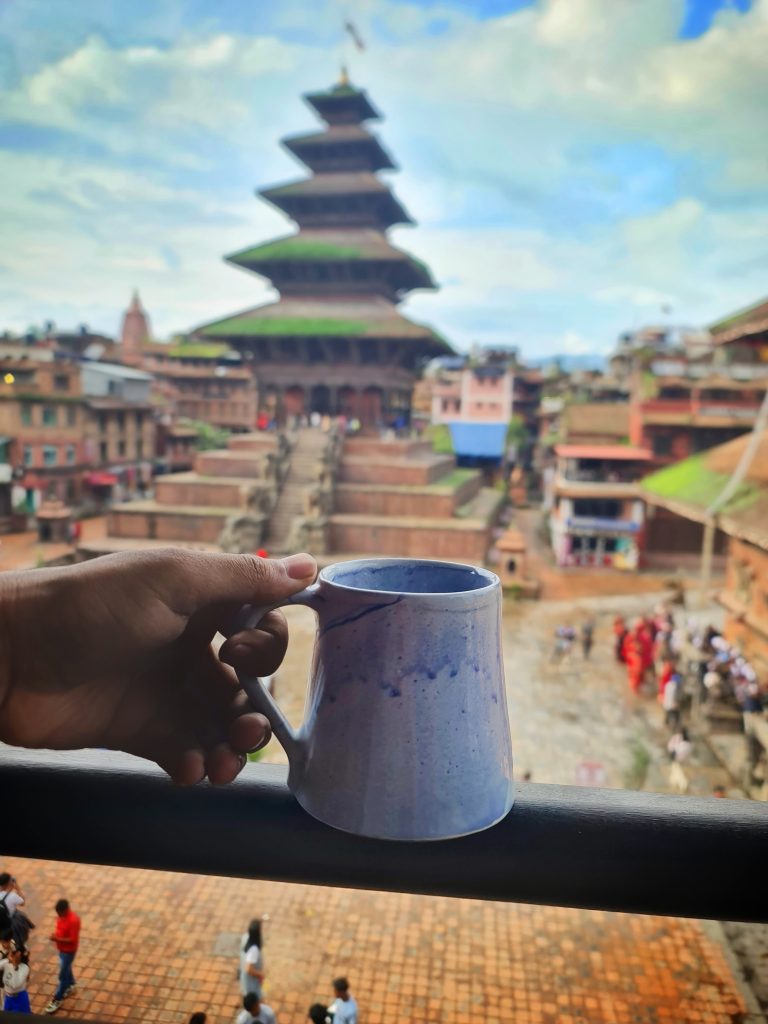 Holding a cup of coffee with Nyatapolo Temple in the background.