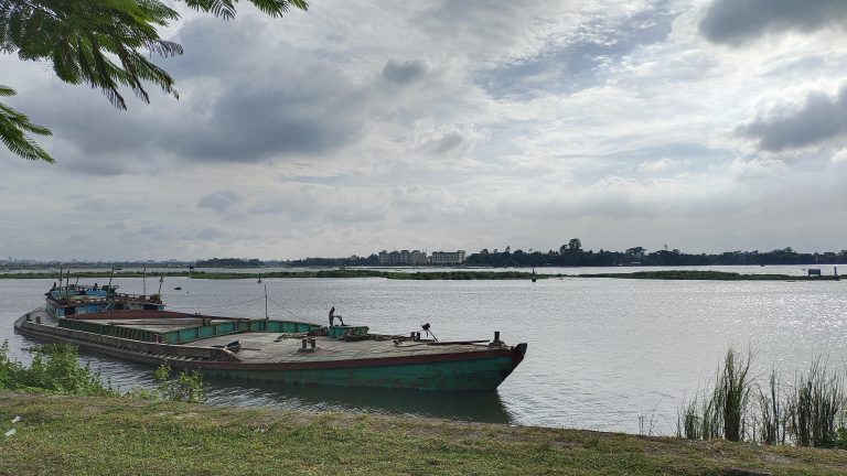 Peaceful river bank scene featuring a boat tied up on the shore, under a cloudy sky.