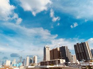 View larger photo: Bangkok cityscape featuring numerous high-rise buildings under a bright blue sky with scattered clouds. The skyline includes a mix of modern skyscrapers and other tall structures in varying designs and colors.