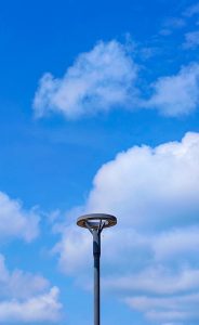  A modern street lamp post stands tall against a bright blue sky with scattered white clouds.