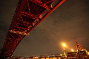 looking up at a red painted bridge from below at night.