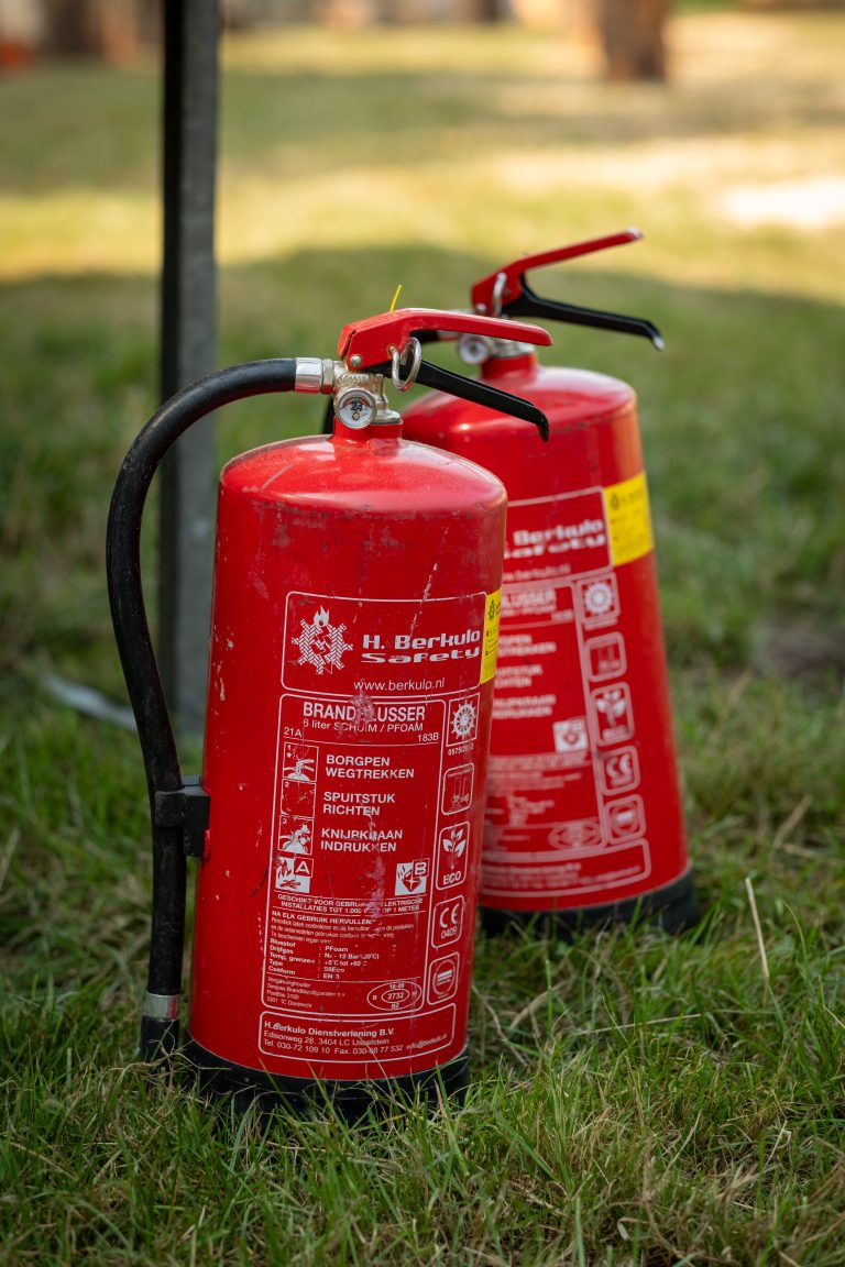 Two fire extinguishers standing in a field of grass.