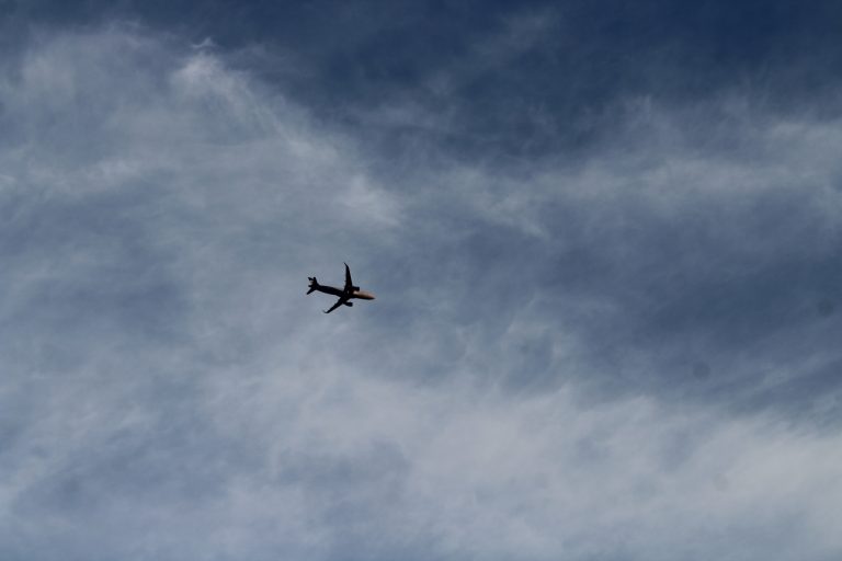 A silhouette of an aeroplane flying high in the sky, surrounded by wispy clouds.