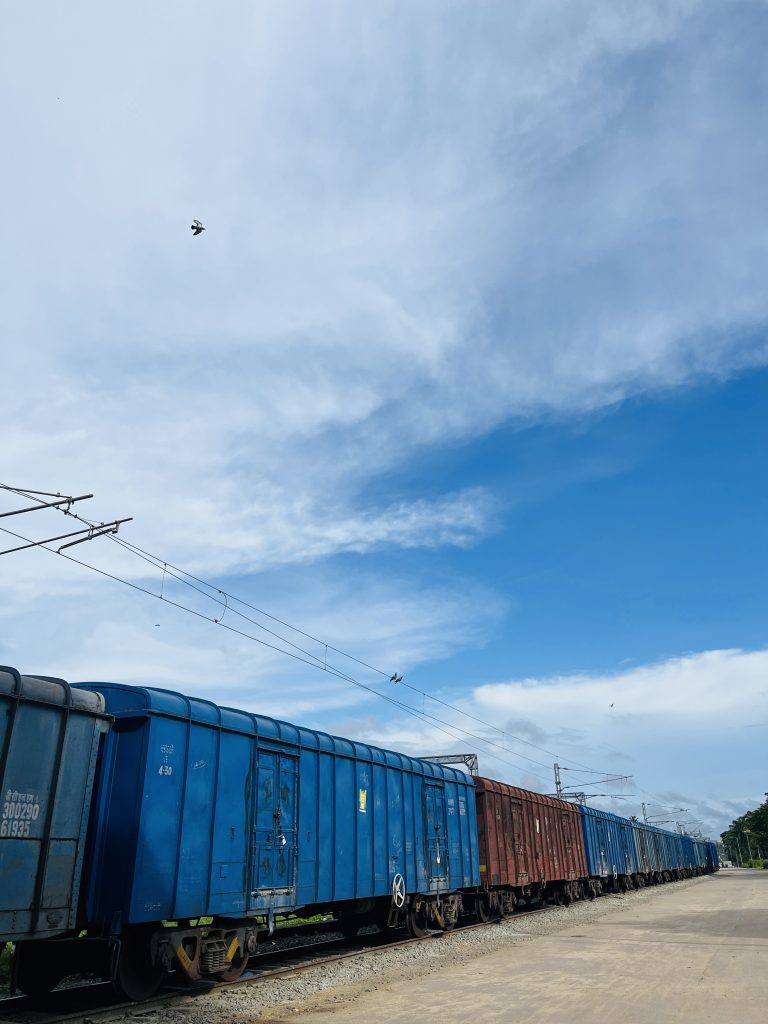 Train cars on a train track. Blue sky overhead with wispy clouds and a bird flying.